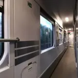 Wnętrze wagonu PKP. Podróż z Lublina do Kołobrzegu. Widok na korytarz i okna, przez które widać rozmyty krajobraz.