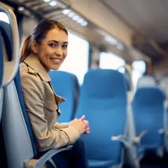Uśmiechnięta kobieta w beżowym płaszczu siedzi w pustym wagonie. Może zapomniała legitymacji w pociągu, ale podróż i tak jest przyjemna.