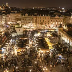 Tłumy ludzi spacerują po rozświetlonym jarmarku bożonarodzeniowym krakow. Wokół stragany, zabytkowe kamienice i Sukiennice.