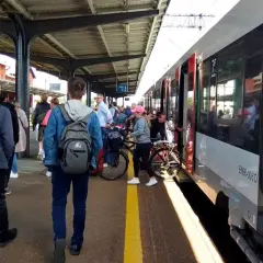 Ludzie czekają na pociąg w Lęborku. W tle widać peron i nowoczesny skład kolejowy.