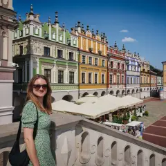 Kobieta w zielonej sukience na tle kolorowych kamienic na Rynku Wielkim w Zamościu. Zamość stare miasto zachwyca architekturą.