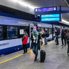 Ludzie z bagażami czekają na pociąg PKP Intercity. Na tablicy informacyjnej widnieje kierunek Kraków Główny. Może to być początek podróży z biletem kredytowym.
