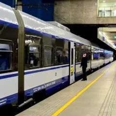 Konduktor czeka przy drzwiach nowoczesnego pociągu PKP Intercity. Malczewski pociąg stoi na peronie, gotowy do podróży.