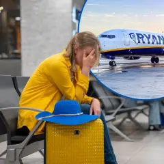 Zmartwiona kobieta w żółtej kurtce czeka na lotnisku na samolot Ryanair. Może to być podróż z Elbląga do Wrocławia.