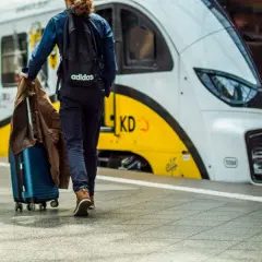 Podróżny z walizką i kurtką idzie w stronę nowoczesnego pociągu. Artus pociąg czeka na pasażerów.