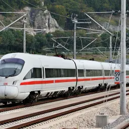 Biały pociąg ICE 5 z czerwonym pasem jedzie po torach, w tle góry i sieć trakcyjna.