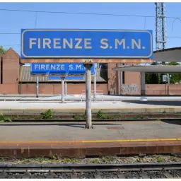 Niebieski znak z napisem "FIRENZE S.M.N." nad peronem na dworcu kolejowym we Florencji.