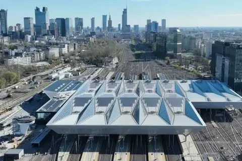 Nowoczesny dach nad peronami największego dworca w Polsce, Warszawy Centralnej, z widokiem na panoramę miasta.