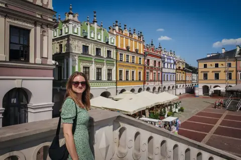 Kobieta w zielonej sukience na tle kolorowych kamienic na Rynku Wielkim w Zamościu. Zamość stare miasto zachwyca architekturą.