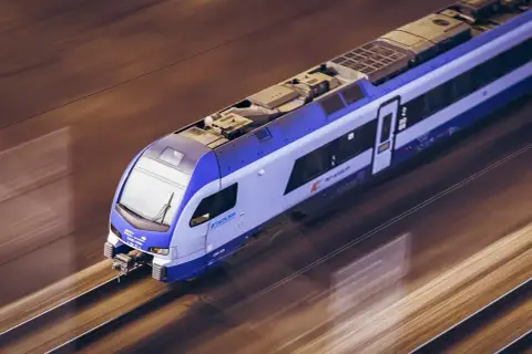 Nowoczesny pociąg IC OSTERWA pędzi po torach, tworząc rozmyte smugi światła i cienia.