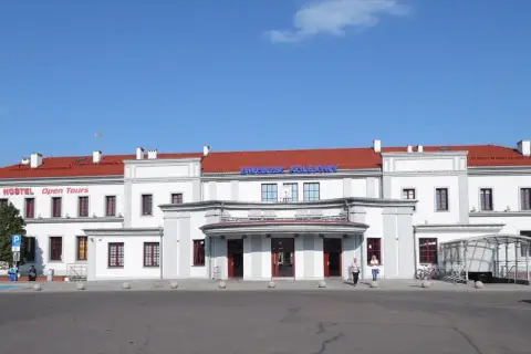 Dworzec PKP Ełk z czerwonym dachem i napisem "Dworzec Kolejowy". Obok hostel "Open Tours".