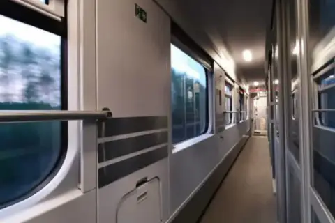 Wnętrze wagonu PKP. Podróż z Lublina do Kołobrzegu. Widok na korytarz i okna, przez które widać rozmyty krajobraz.