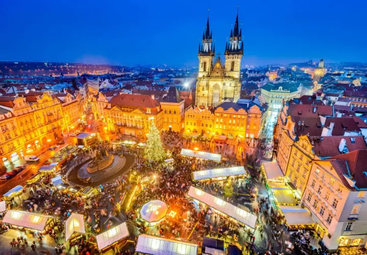 Tłoczny jarmark bożonarodzeniowy w Pradze, z oświetloną choinką i zabytkową architekturą w tle.