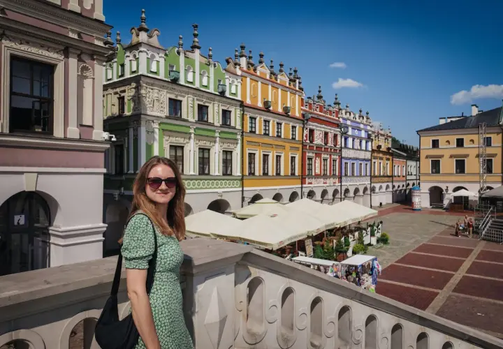Kobieta w zielonej sukience na tle kolorowych kamienic na Rynku Wielkim w Zamościu. Zamość stare miasto zachwyca architekturą.
