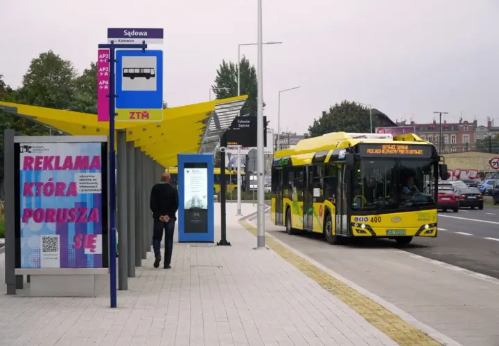 Dworzec autobusowy Katowice Sądowa. Żółty autobus elektryczny zatrzymuje się na przystanku. Rozkład jazdy widoczny na tablicy informacyjnej.