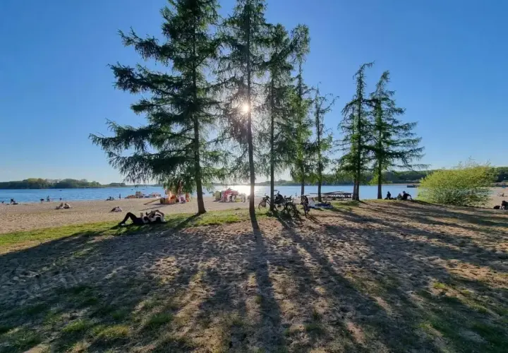 Słoneczny dzień nad jeziorem, ludzie odpoczywają na plaży, rowery czekają. Skorzęcin atrakcje to idealne miejsce na relaks.