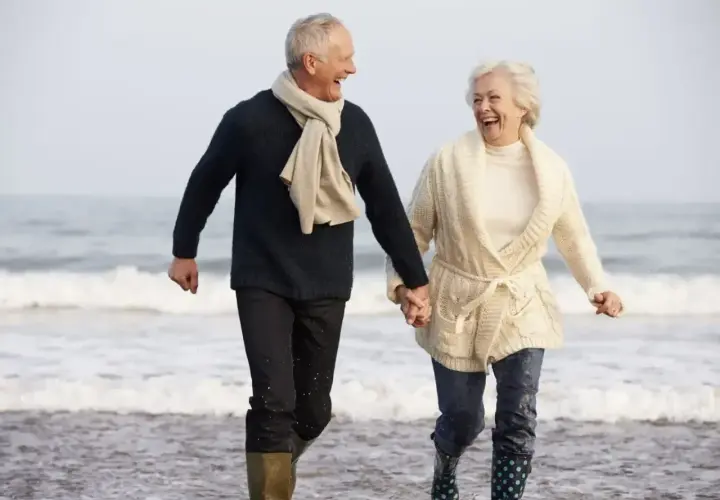 Szczęśliwa para seniorów biegnie plażą, trzymając się za ręce. Idealne tanie wycieczki dla seniorów, by poczuć radość życia!