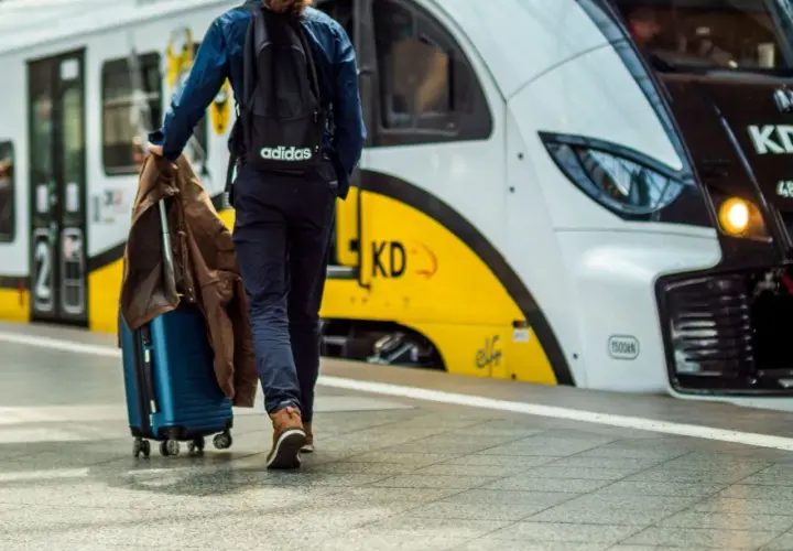 Podróżny z walizką i kurtką idzie w stronę nowoczesnego pociągu. Artus pociąg czeka na pasażerów.
