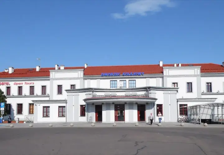 Dworzec PKP Ełk z czerwonym dachem i napisem "Dworzec Kolejowy". Obok hostel "Open Tours".