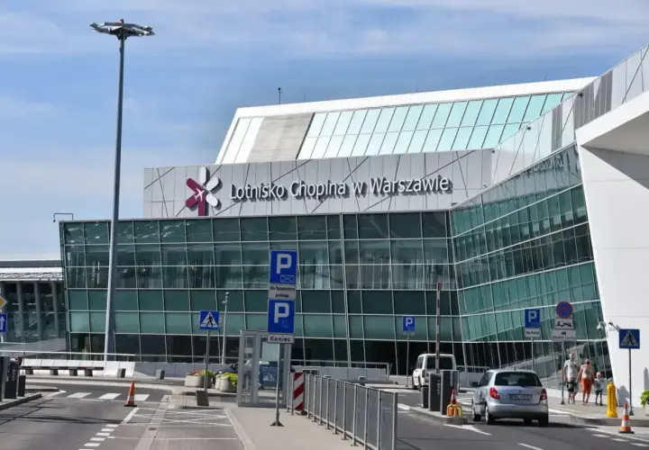 Nowoczesny budynek Lotniska Chopina w Warszawie z charakterystycznym logo. Samochody podjeżdżają do terminala.