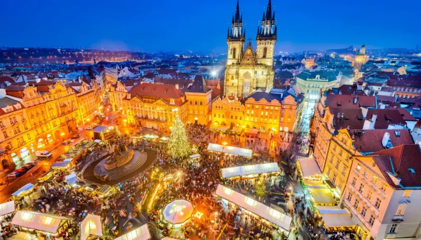 Tłoczny jarmark bożonarodzeniowy w Pradze, z oświetloną choinką i zabytkową architekturą w tle.