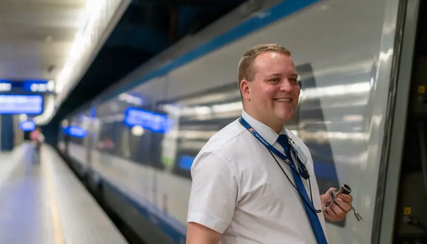 Uśmiechnięty mężczyzna w białej koszuli i granatowym krawacie, z identyfikatorem PKP Intercity, trzymający klucz. To jego pierwszy dzień po kursie na konduktora Intercity.