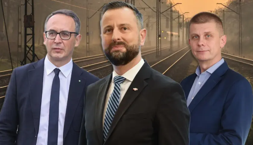 Trzech mężczyzn w garniturach na tle torów kolejowych. Jeden z nich, z brodą, wygląda jak prezes PKP.