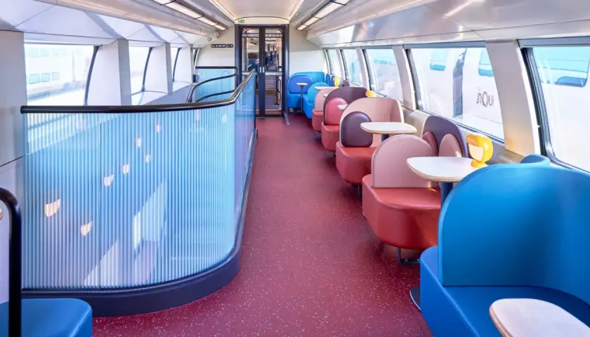 Wnętrze pociągu TGV inOui z kolorowymi siedzeniami i stolikami.
