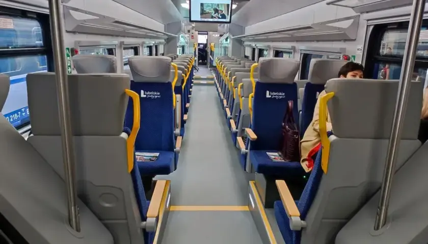Wnętrze szynobusu na trasie Lublin - Zamość. Puste, niebieskie siedzenia z żółtymi uchwytami czekają na pasażerów.
