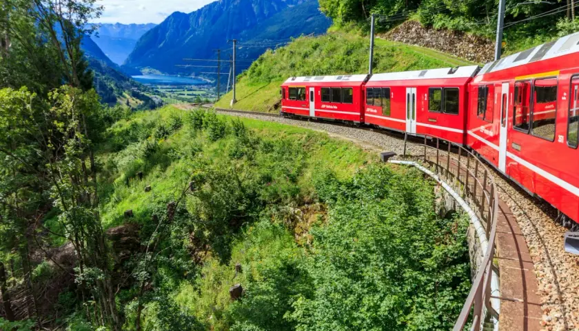 Czerwony pociąg jedzie przez malownicze szwajcarskie góry. Sprawdź swiss travel pass cena, by odkryć te widoki!