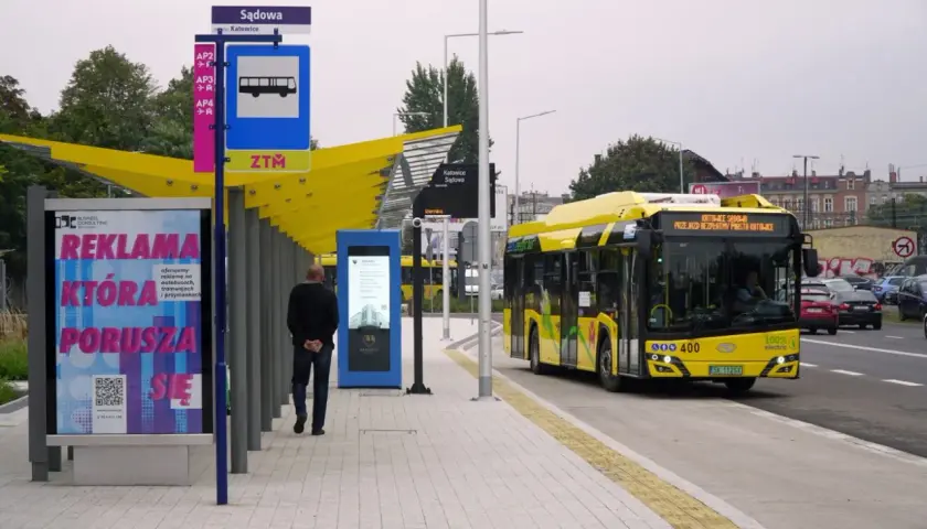 Dworzec autobusowy Katowice Sądowa. Żółty autobus elektryczny zatrzymuje się na przystanku. Rozkład jazdy widoczny na tablicy informacyjnej.