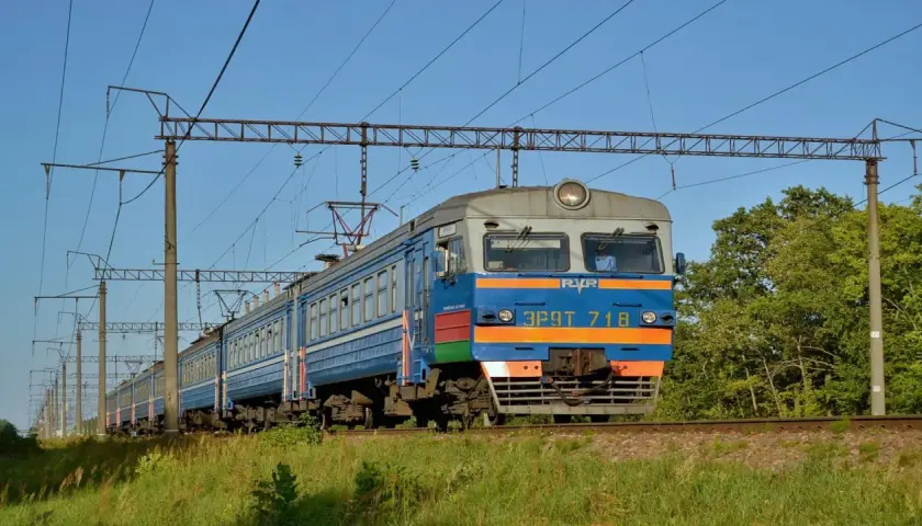 Pociąg elektryczny jedzie po torach, a nad nim widać sieć trakcyjną. To idealny sposób, jak dojechać pociągiem do Kamienia Pomorskiego.