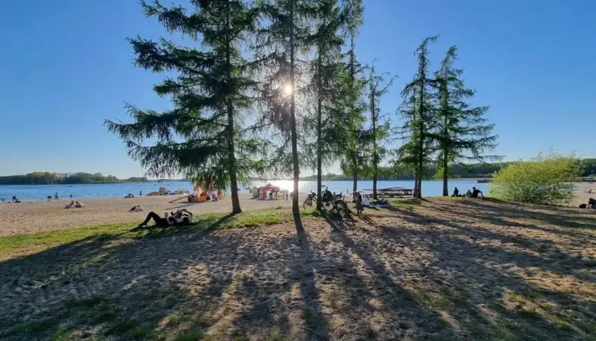 Słoneczny dzień nad jeziorem, ludzie odpoczywają na plaży, rowery czekają. Skorzęcin atrakcje to idealne miejsce na relaks.