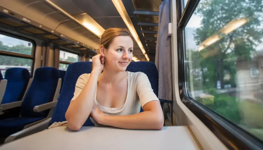 Uśmiechnięta kobieta podróżuje szynobusem, patrząc przez okno na mijany krajobraz.