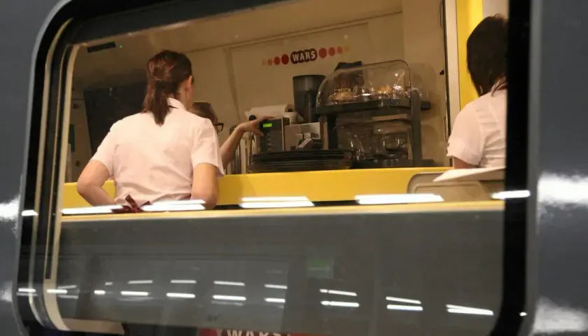 Wnętrze wagonu restauracyjnego z obsługą przygotowującą napoje.