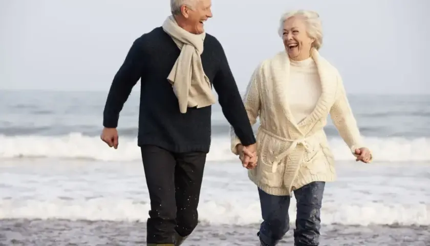 Szczęśliwa para seniorów biegnie plażą, trzymając się za ręce. Idealne tanie wycieczki dla seniorów, by poczuć radość życia!