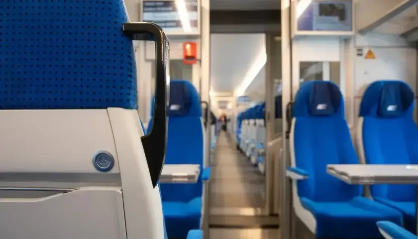 Wnętrze pociągu PKP Intercity. Siedzenia w kolorze niebieskim, rzędy foteli po obu stronach korytarza.