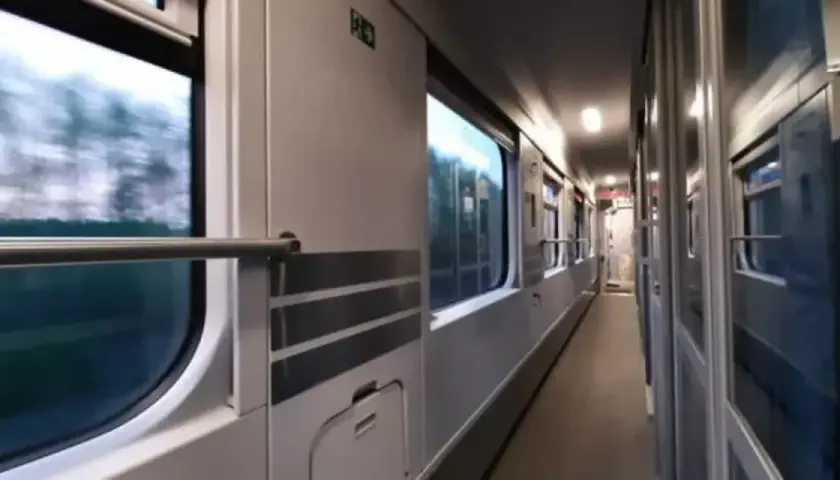 Wnętrze wagonu PKP. Podróż z Lublina do Kołobrzegu. Widok na korytarz i okna, przez które widać rozmyty krajobraz.