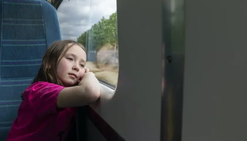 Zamyślona dziewczynka w różowej bluzce patrzy przez okno pociągu. Czy 12 latek może sam jechać pociągiem?