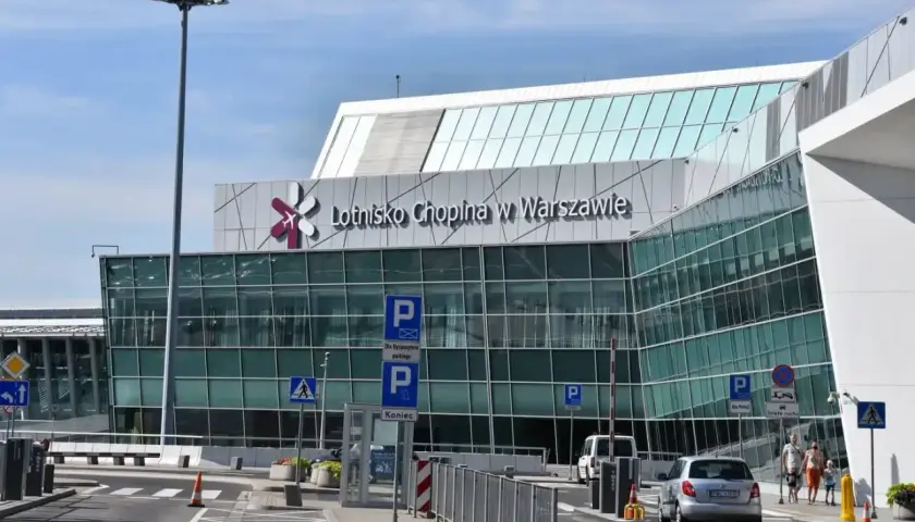 Nowoczesny budynek Lotniska Chopina w Warszawie z charakterystycznym logo. Samochody podjeżdżają do terminala.