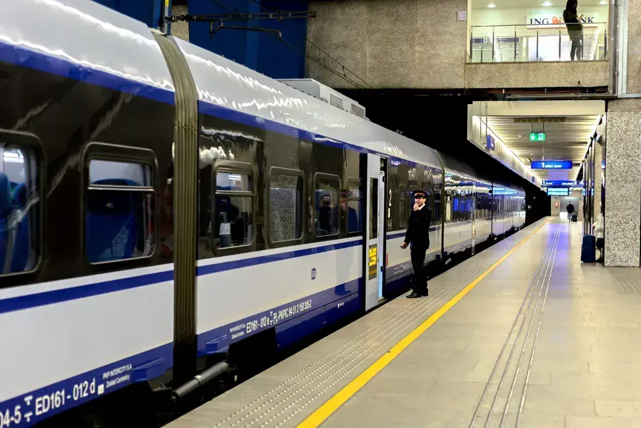 Konduktor czeka przy drzwiach nowoczesnego pociągu PKP Intercity. Malczewski pociąg stoi na peronie, gotowy do podróży.