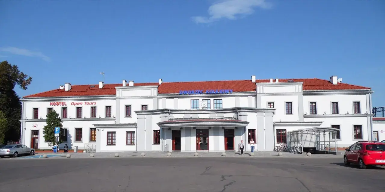 Dworzec PKP Ełk z czerwonym dachem i napisem "Dworzec Kolejowy". Obok hostel "Open Tours".