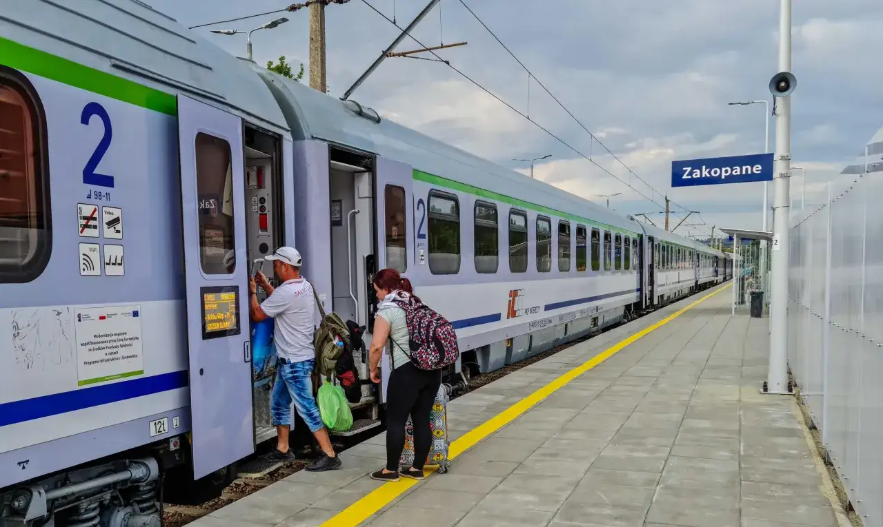 Ludzie wsiadają do pociągu PKP Intercity z bagażami. Na peronie widać tabliczkę 