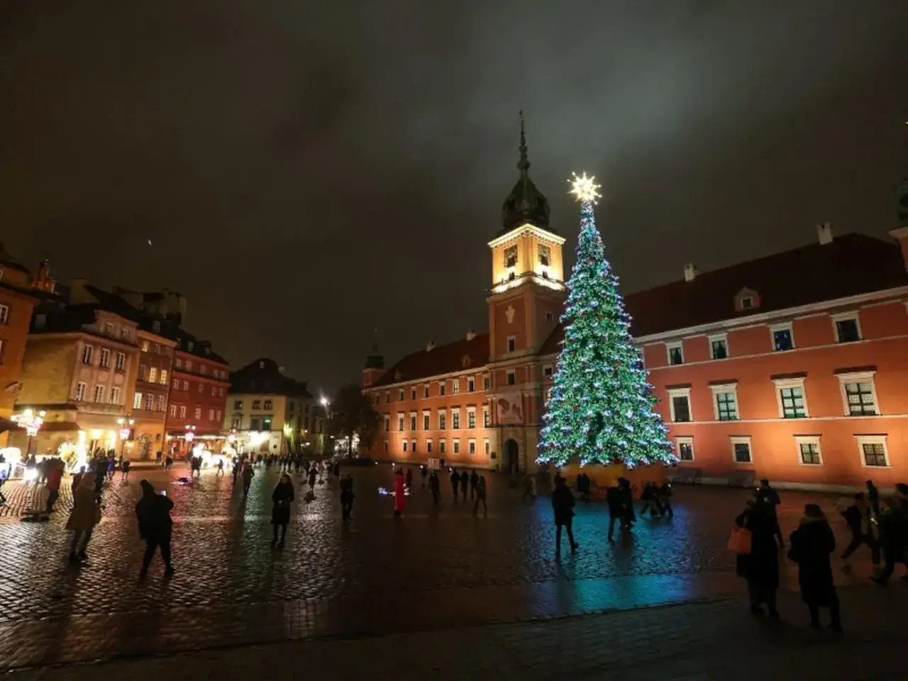 Nocny jarmark świąteczny Warszawa. Plac Zamkowy rozświetla choinka, ludzie spacerują wśród kamienic.