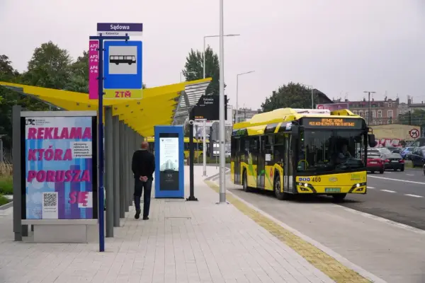 Dworzec autobusowy Katowice Sądowa. Żółty autobus elektryczny zatrzymuje się na przystanku. Rozkład jazdy widoczny na tablicy informacyjnej.