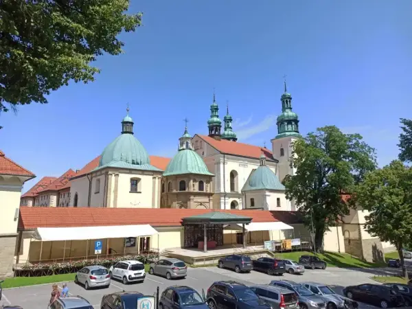 Kraków Kalwaria Zebrzydowska: barokowy zespół klasztorny z zielonymi kopułami i wieżami, otoczony parkingiem i drzewami.